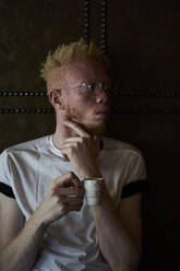 Albino man holding a cup of coffee and looking sideways - VEGF01665