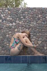 Portrait of young tattooed woman relaxing at poolside - AFVF05577