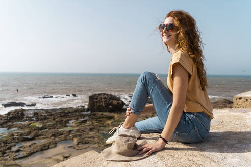 Porträt einer glücklichen jungen Frau, die das Sonnenlicht am Meer genießt, Essaouira, Marokko - AFVF05593