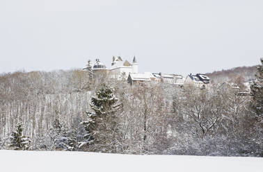 Deutschland, Nordrhein-Westfalen, Hellenthal, Schneebedeckter Wald vor ländlichem Dorf mit Schloss Wildenburg im Hintergrund - GWF06507