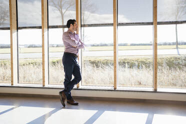 Businessman looking out of window in open-plan office - DIGF09400