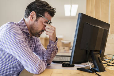 Tired businessman at desk in wooden open-plan office - DIGF09403