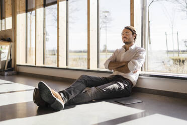 Businessman with closed eyes sitting at the window in open-plan office - DIGF09405