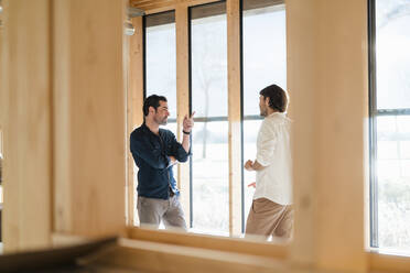 Two businessmen talking at the window in wooden open-plan office - DIGF09410