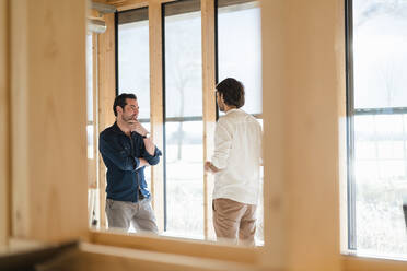 Two businessmen talking at the window in wooden open-plan office - DIGF09411