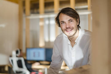 Portrait of smiling businessman in wooden open-plan office - DIGF09429