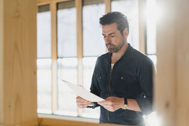 Businessman reading document in wooden open-plan office - DIGF09430