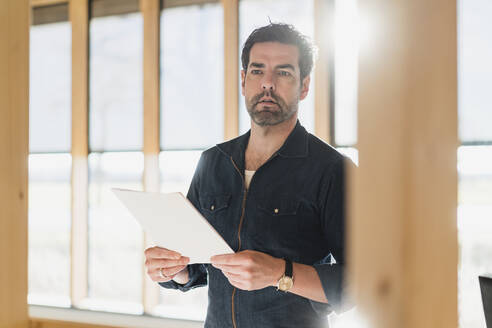 Businessman holding document in wooden open-plan office - DIGF09431