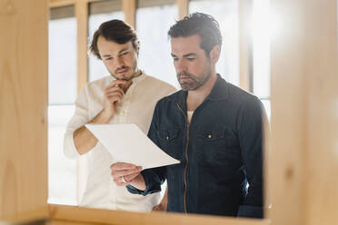 Two businessmen with document in wooden open-plan office - DIGF09432