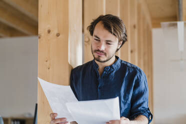 Businessman reading document in wooden open-plan office - DIGF09442