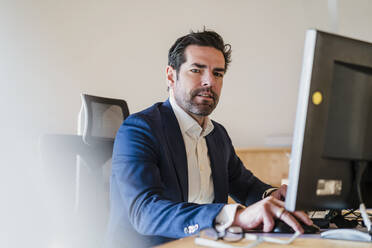 Portrait of businessman sitting at desk in wooden open-plan office - DIGF09450