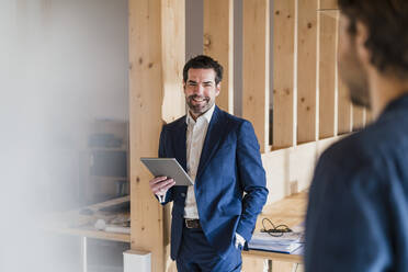 Smiling businessman holding tablet in wooden open-plan office - DIGF09455