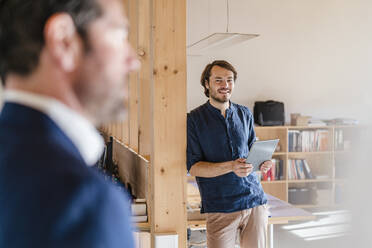 Smiling businessman holding tablet in wooden open-plan office - DIGF09457