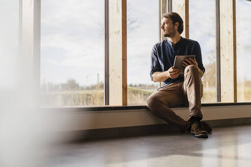 Geschäftsmann mit Tablet und Blick aus dem Fenster in einem Großraumbüro - DIGF09459