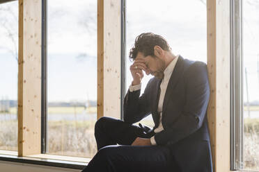 Tired businessman sitting at the window in office - DIGF09462