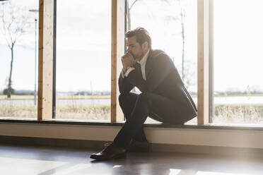 Serious businessman sitting at the window in office - DIGF09463