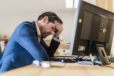 Frustrierter Geschäftsmann sitzt am Schreibtisch im Büro - DIGF09469