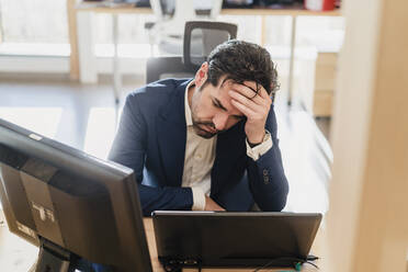 Frustrated businessman sitting at desk in office - DIGF09471