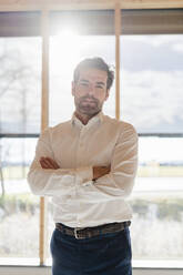 Portrait of confident businessman at the window in open-plan office - DIGF09474