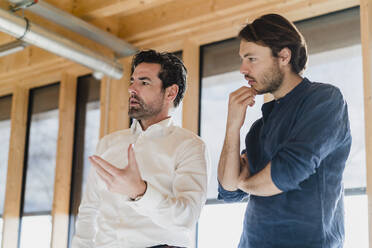 Two businessmen talking in wooden open-plan office - DIGF09475