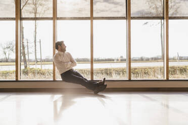 Businessman sitting at the window in open-plan office - DIGF09482