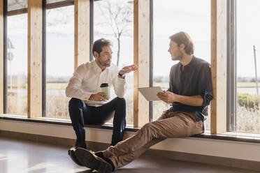 Zwei Geschäftsleute mit Tablet im Gespräch am Fenster in einem Großraumbüro - DIGF09484