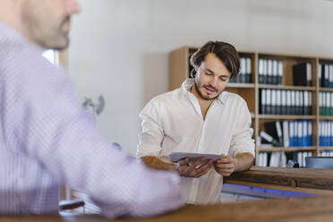 Businessman reading document in wooden open-plan office - DIGF09500