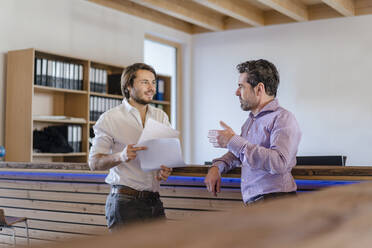 Zwei Geschäftsleute mit Dokumenten im Gespräch in einem hölzernen Großraumbüro - DIGF09501