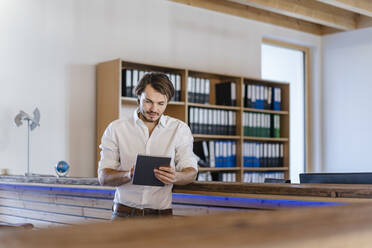 Businessman using tablet in wooden open-plan office - DIGF09502