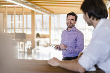 Two businessmen talking in wooden open-plan office - DIGF09507