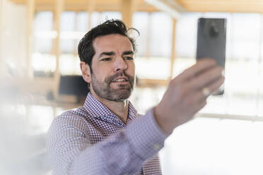 Geschäftsmann macht ein Selfie in einem Großraumbüro aus Holz - DIGF09523