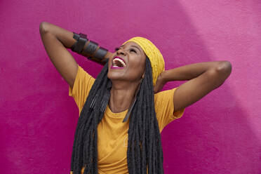 Portrait of woman with long dreadlocks laughing in front of a pink wall - VEGF01679