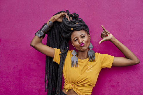 Portrait of woman with long dreadlocks making shaka sign in front of a pink wall - VEGF01685