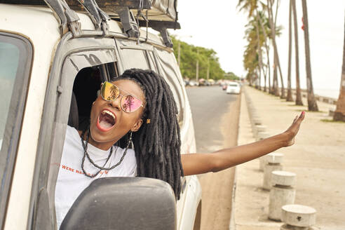 Porträt einer schreienden Frau mit Dreadlocks, die sich aus dem Autofenster lehnt, Maputo, Mosambik - VEGF01693