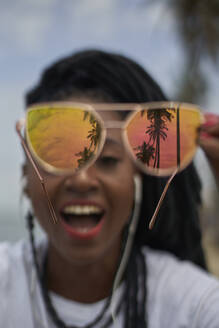 Frau zeigt Reflexion von Palmen auf ihrer verspiegelten Sonnenbrille - VEGF01697