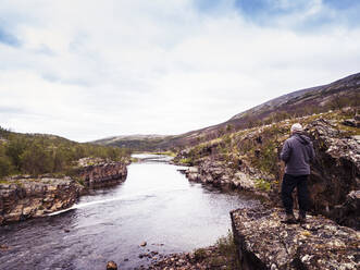 Norwegen, Troms og Finnmark, Lakselv, Männlicher Wanderer bewundert den Blick auf den Fluss und die umliegende Landschaft - DHEF00136