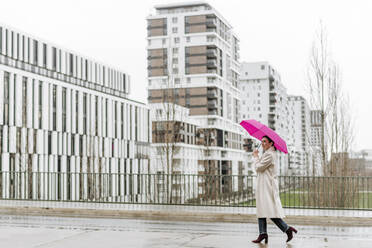 Lächelnde Frau mit rosa Regenschirm beim Spaziergang in der Stadt - VYF00050