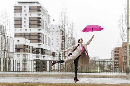 Smiling woman with pink umbrella walking in the city - VYF00051
