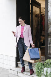 Stylische Frau in rosa Jacke mit Einkaufstüten und Smartphone - VYF00054