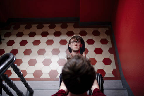Spiegelbild eines ernsten jungen Mannes auf einer Treppe sitzend - OGF00208