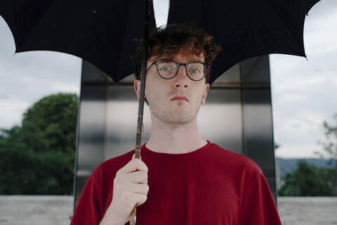Porträt eines ernsten jungen Mannes mit Regenschirm, Kassel, Deutschland, lizenzfreies Stockfoto