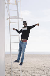Stylish young man standing on ladder at the beach - MPPF00612
