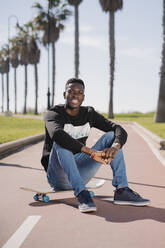 Porträt eines lächelnden jungen Mannes, der auf einem Skateboard sitzt - MPPF00632