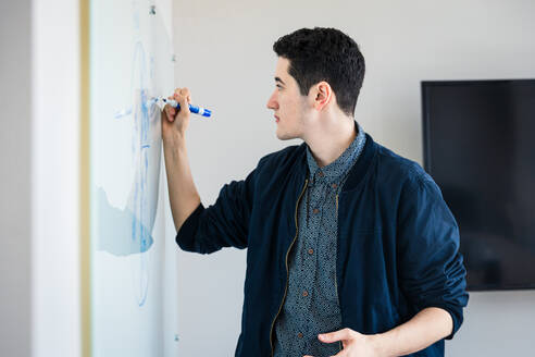 Junger Unternehmer, der während einer Sitzung im Sitzungssaal auf ein Whiteboard schreibt - CAVF76458