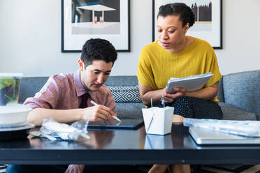 Businesswoman looking at male colleague using graphics tablet while sitting at table in office - CAVF76479