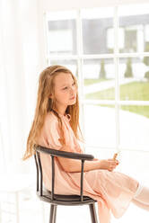 Mädchen sitzt zu Ostern in einem Hochstuhl am Fenster - CAVF76589