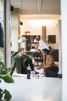 Glückliche Architekten im Gespräch, während eine Unternehmerin im Hintergrund zu Hause arbeitet - MASF16871