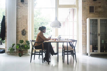 Female architect using phone while sitting by table at home - MASF16887