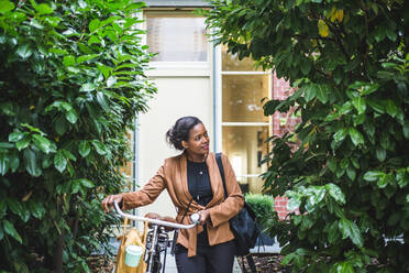 Lächelnde Architektin schaut weg, während sie mit dem Fahrrad vor einem Haus steht - MASF16923