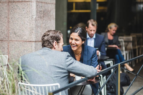 Happy businesswoman sitting with coworker at sidewalk cafe stock photo